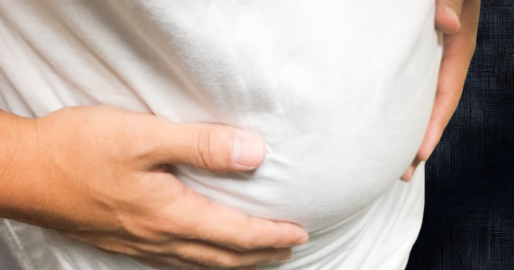 お腹に手を当てる太った男性の画像
