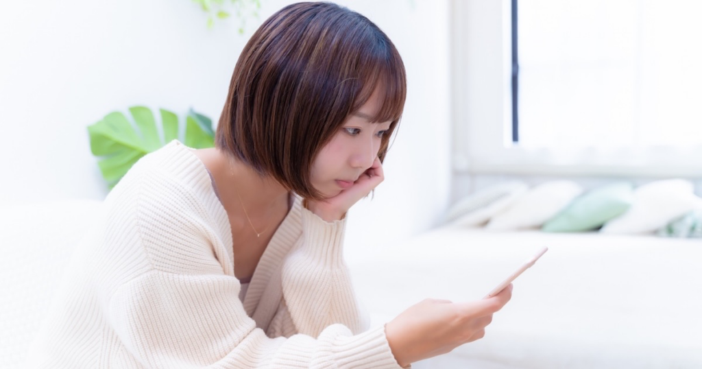 スマホを見ながら考える女性
